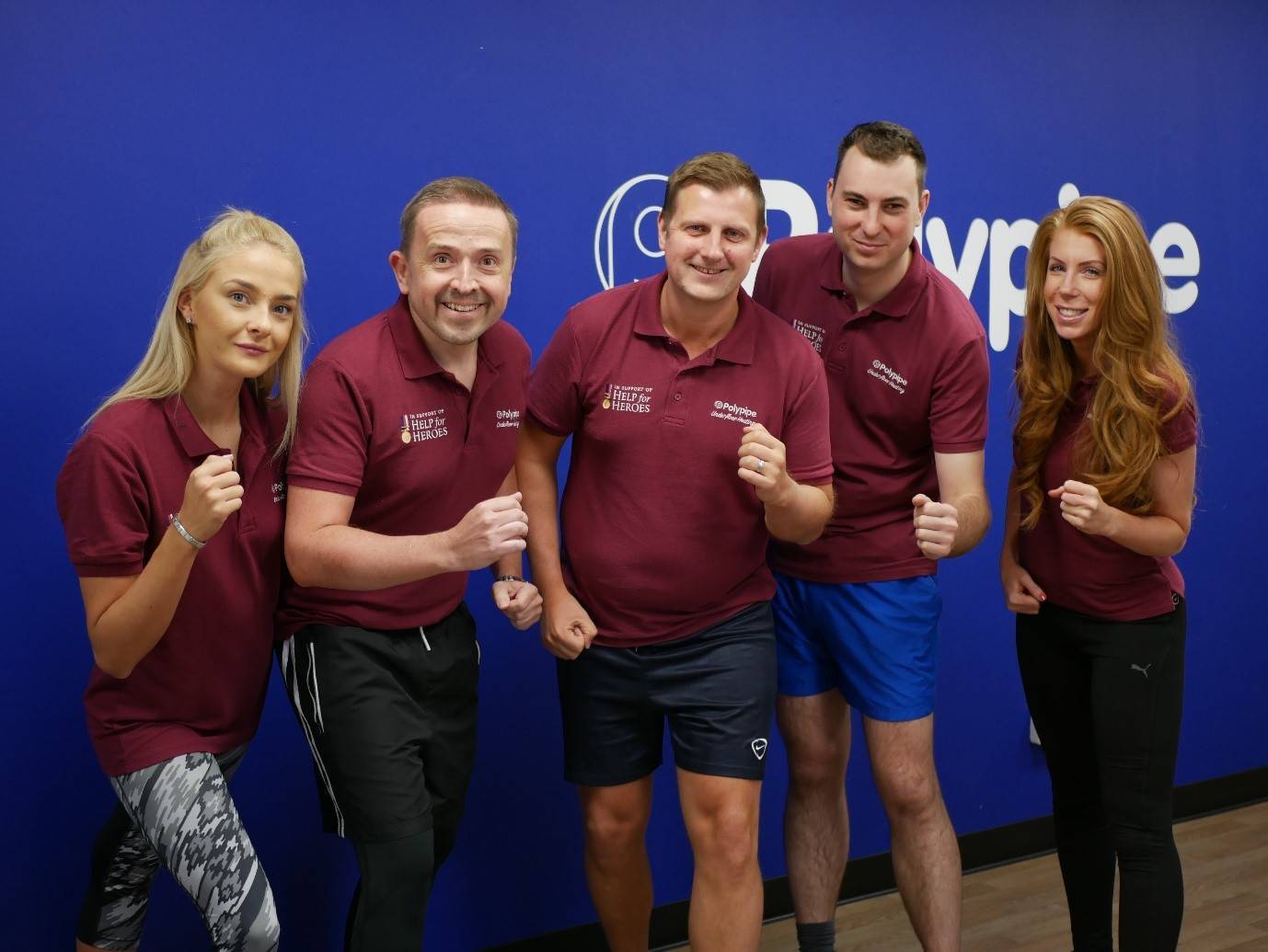 The Polypipe Underfloor Heating technical office team stand in a runners pose in front of a Polypipe logo.